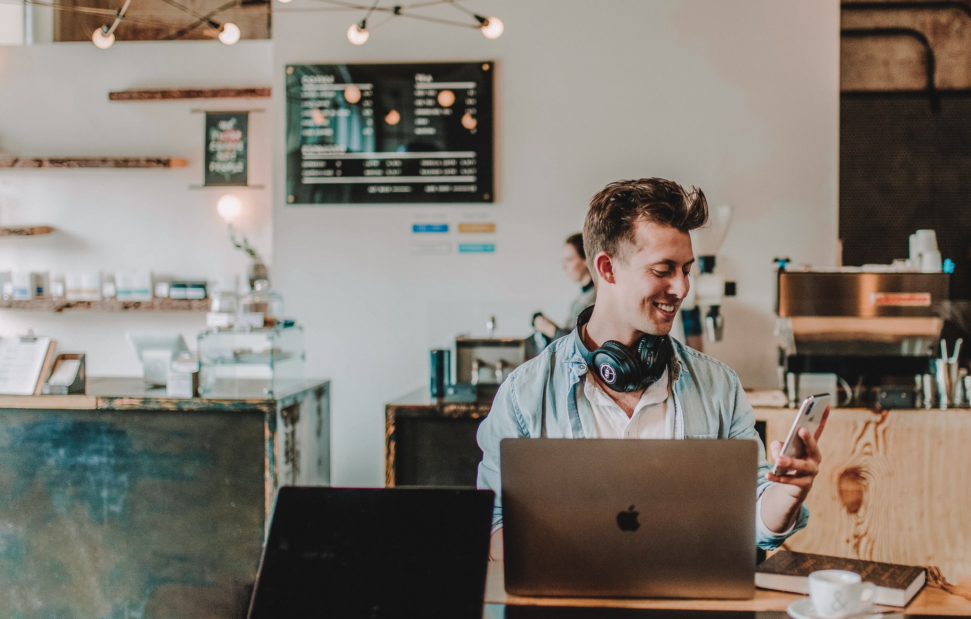 Male at a coffee shop smiling at the phone while working on the computer